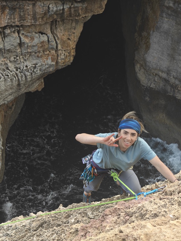 Agnieszka climbing a rock face, flashing a peace sign