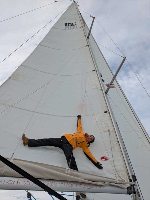 Agnieszka hanging off a sailboat mast in foul weather gear